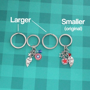 K&ouml;nnte beinhalten: Schl&uuml;sselanh&auml;nger mit silbernen Schl&uuml;sselringen und Anh&auml;ngern. Ein Schl&uuml;sselanh&auml;nger hat einen Captain America Schild-Anh&auml;nger, einen Stern-Anh&auml;nger, eine blaue Perle und einen Herz-Anh&auml;nger mit "PART I CR". Der andere Schl&uuml;sselanh&auml;nger hat einen Stern-Anh&auml;nger, eine rote Perle, einen Herz-Anh&auml;nger mit "NERS N IME" und einen Anh&auml;nger mit einem roten Stern.