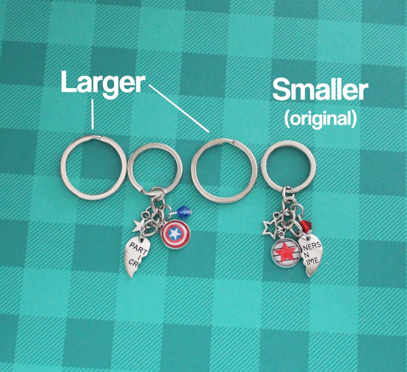 K&ouml;nnte beinhalten: Schl&uuml;sselanh&auml;nger mit silbernen Schl&uuml;sselringen und Anh&auml;ngern. Ein Schl&uuml;sselanh&auml;nger hat einen Captain America Schild-Anh&auml;nger, einen Stern-Anh&auml;nger, eine blaue Perle und einen Herz-Anh&auml;nger mit "PART I CR". Der andere Schl&uuml;sselanh&auml;nger hat einen Stern-Anh&auml;nger, eine rote Perle, einen Herz-Anh&auml;nger mit "NERS N IME" und einen Anh&auml;nger mit einem roten Stern.