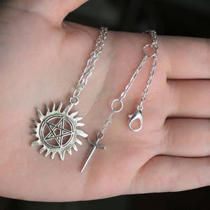 K&ouml;nnte beinhalten: Silberne Halskette mit einem Pentagramm-Anh&auml;nger in einem Kreis und einem Schwertanh&auml;nger.