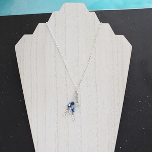 May include: A silver chain necklace with a silver hammer charm and blue crystal beads. The necklace is displayed on a white wooden stand.