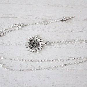 K&ouml;nnte beinhalten: Eine silberne Halskette mit einem Pentagramm-Anh&auml;nger in einem Sonnensymbol. Die Kette hat eine silberne Kette und einen kleinen silbernen Schwertanh&auml;nger.