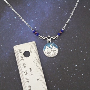 May include: A silver necklace with a blue and white mountain scene pendant. The pendant is surrounded by five silver stars and blue beads. The necklace is 18 inches long.