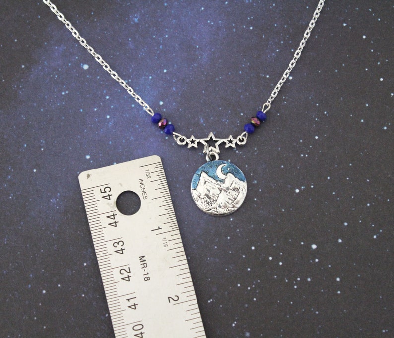 May include: A silver necklace with a blue and white mountain scene pendant. The pendant is surrounded by five silver stars and blue beads. The necklace is 18 inches long.