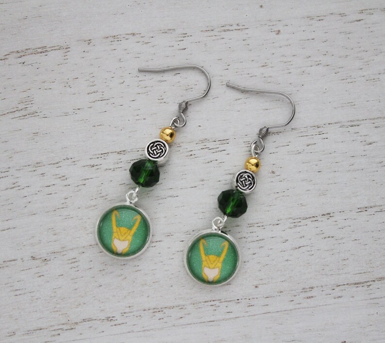 以下が含まれることがあります： 緑と黄色のデザイン、シルバー仕上げ、緑と金のビーズアクセント、シルバーフックが特徴のぶら下がりピアス。ピアスには円形のペンダントが付いています。