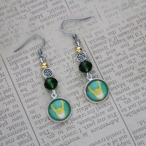 以下が含まれることがあります： シルバーカラーのぶら下がりピアス。緑とゴールドのアクセントが特徴です。各ピアスには、ターコイズ色の背景に黄色のデザインが施された丸いチャーム、緑色のビーズ、ケルトノットのディテールが施されています。ユニークなアクセサリーです。