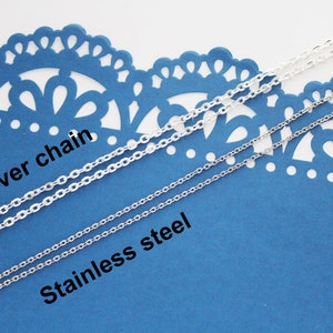 May include: Two silver chains on a blue background. The top chain is labeled "Silver chain" and the bottom chain is labeled "Stainless steel".