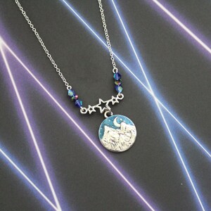 May include: A silver necklace with a blue and white enamel pendant featuring a crescent moon and mountains. The necklace is adorned with blue crystal beads and silver star charms.