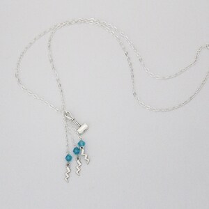 May include: Silver chain necklace with a silver hammer charm and three blue crystal beads hanging from it.