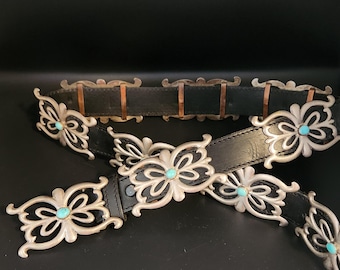 May include: Two black leather belts with silver-tone butterfly-shaped buckles and turquoise-colored stone accents. The belts have copper-colored metal accents and are displayed against a dark background.