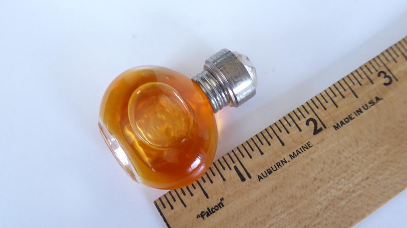 K&ouml;nnte beinhalten: Ein runder, durchscheinender bernsteinfarbener Glasknauf mit einem silberfarbenen Metallsockel und einem Gewindeanschluss, platziert neben einem Holzlineal, das eine Breite von etwa 4,5 cm f&uuml;r das Glasteil anzeigt.