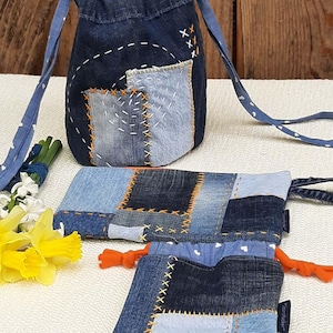 Könnte beinhalten: Drei Beutel aus Jeans in verschiedenen Größen, alle aus Patchwork-Jeansstoff mit orangefarbenen Nähten. Die größte Tasche hat einen Kordelzug und einen langen Riemen. Die kleinste Tasche hat einen Kordelzug und einen kleinen orangefarbenen Quasten. Alle Taschen haben ein weißes Herzmuster im Inneren.