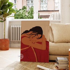Puede incluir: Una ilustraci&oacute;n digital de una mujer con cabello largo y oscuro, vestida con un sari rojo y dorado, con la cabeza apoyada en el brazo. La ilustraci&oacute;n est&aacute; enmarcada y se exhibe en una pared de una sala de estar.