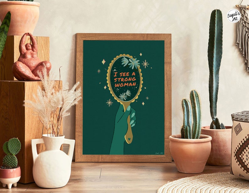 artwork of a quote "i see a strong woman" is written on a mirror held by a woman hand, this artwork is in emerald green in color .it is a vertical poster