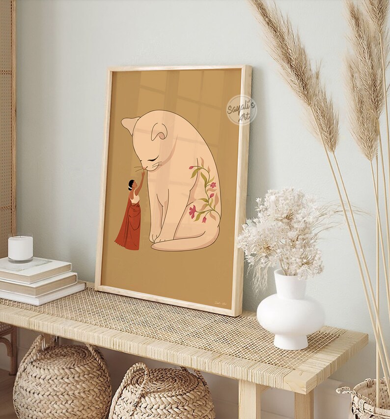 Pode incluir: Uma ilustra&ccedil;&atilde;o emoldurada de uma mulher em um sari vermelho e dourado tocando o nariz de um gato grande de cor rosa claro com tatuagens florais. O fundo &eacute; de cor marrom claro. O texto "Sayali's Art" est&aacute; no canto superior direito da imagem.