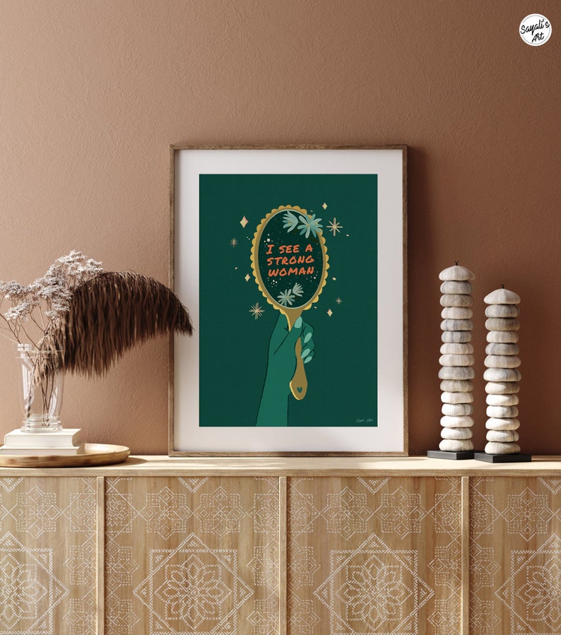 artwork of a quote "i see a strong woman" is written on a mirror held by a woman hand, this artwork is in emerald green in color .it is a vertical poster