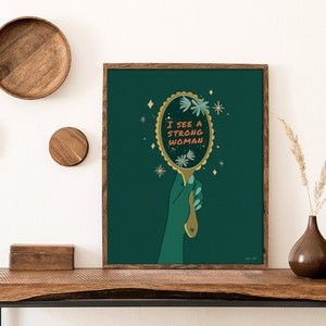 artwork of a quote "i see a strong woman" is written on a mirror held by a woman hand, this artwork is in emerald green in color .it is a vertical poster