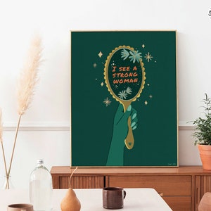 artwork of a quote "i see a strong woman" is written on a mirror held by a woman hand, this artwork is in emerald green in color .it is a vertical poster