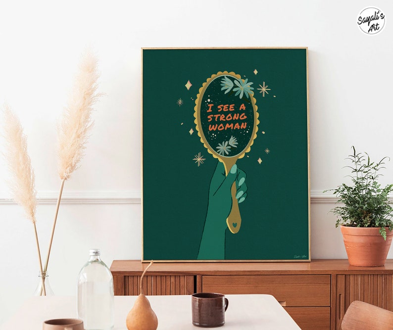 artwork of a quote "i see a strong woman" is written on a mirror held by a woman hand, this artwork is in emerald green in color .it is a vertical poster