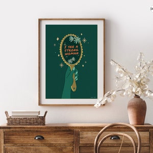 artwork of a quote "i see a strong woman" is written on a mirror held by a woman hand, this artwork is in emerald green in color .it is a vertical poster