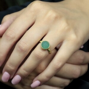 May include: A gold ring with a round green gemstone. The ring is on a person's finger.