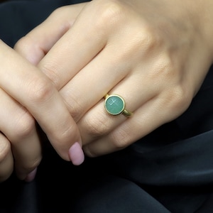 May include: A gold ring with a round, light green gemstone.