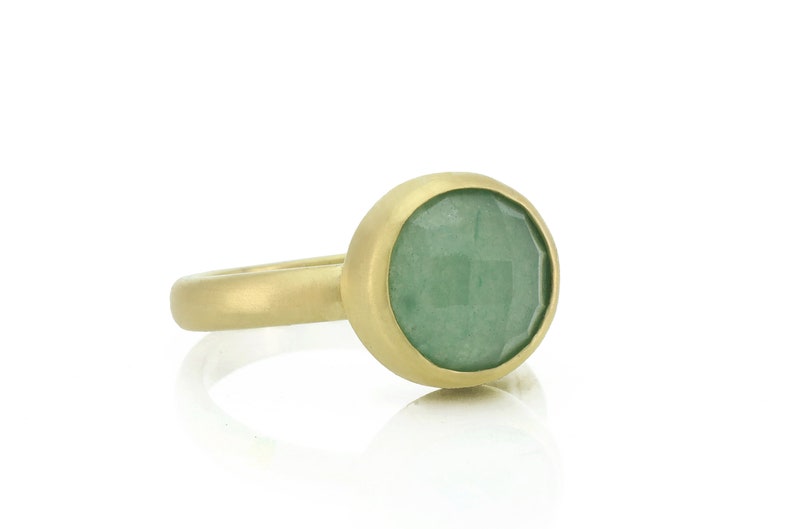 May include: A gold ring with a green gemstone set in a bezel setting.