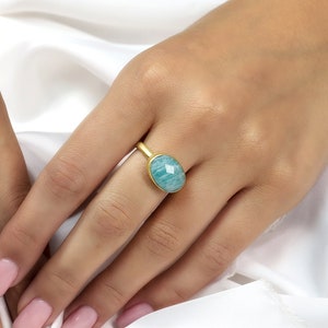 Puede incluir: Un anillo de oro con una piedra ovalada de color azul claro. El anillo est&aacute; en un dedo.