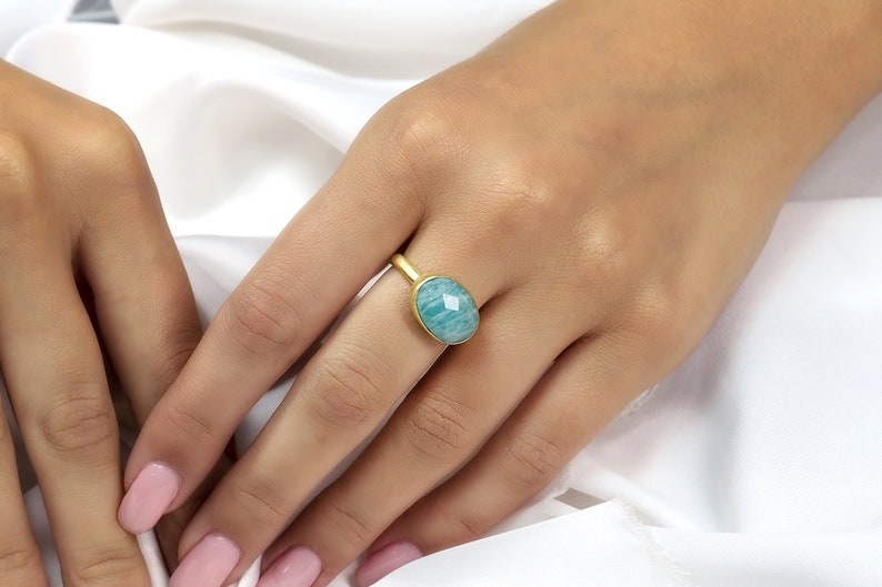 Puede incluir: Un anillo de oro con una piedra ovalada de color azul claro. El anillo est&aacute; en un dedo.