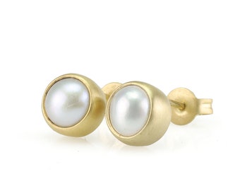 May include: A pair of gold pearl stud earrings. Each earring features a white pearl set in a gold setting.