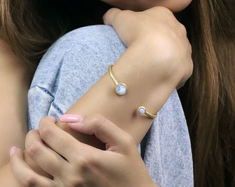 Pode incluir: Um bracelete de punho dourado com dois acentos de pedra da lua redondos. O bracelete é aberto e ajustável.