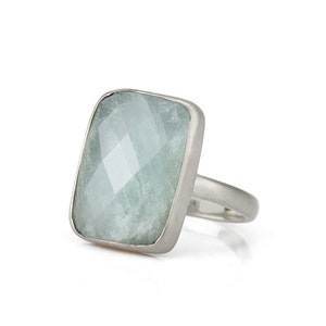 May include: A silver ring with a large, light blue, faceted gemstone set in a rectangular bezel.