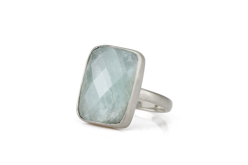 May include: A silver ring with a large, light blue, faceted gemstone set in a rectangular bezel.