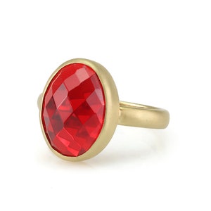 May include: A gold ring with a large, red, faceted gemstone.