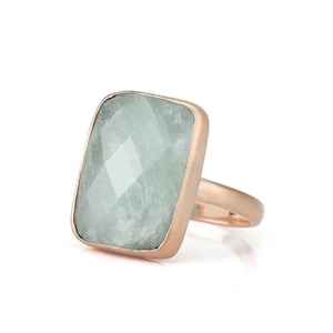 May include: A rose gold ring with a large, rectangular, light green gemstone.