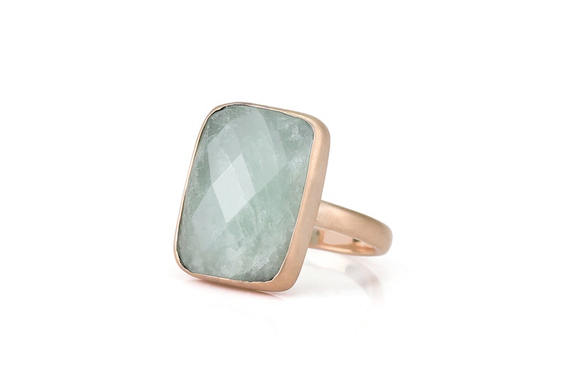 May include: A rose gold ring with a large, rectangular, light green gemstone.