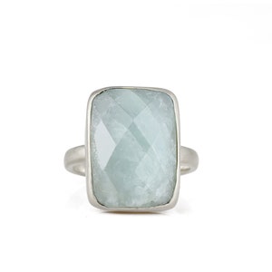 May include: A silver ring with a large, light blue, faceted gemstone set in a rectangular bezel.