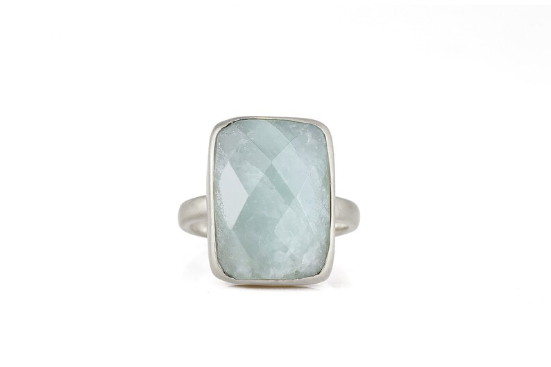 May include: A silver ring with a large, light blue, faceted gemstone set in a rectangular bezel.