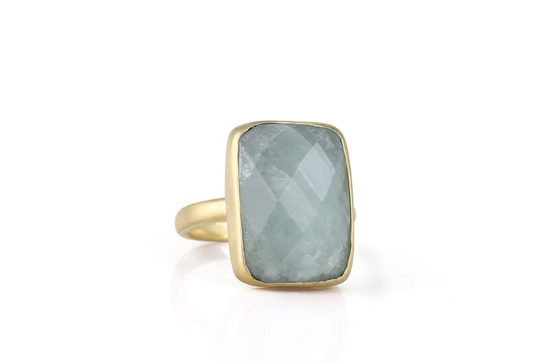 May include: A gold ring with a large, rectangular, light blue gemstone. The gemstone has a faceted cut.