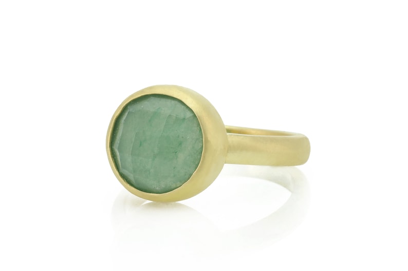May include: A gold ring with a green gemstone set in a bezel setting. The ring has a smooth, rounded band.