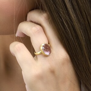 May include: A gold ring with a large, oval-shaped, faceted, pink gemstone.