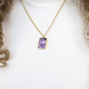 Puede incluir: Un collar de cadena dorada con un colgante rectangular con una piedra preciosa púrpura facetada.