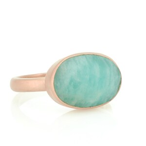 Puede incluir: Un anillo de oro rosa con una gran piedra preciosa ovalada de color verde. La piedra preciosa es de color verde claro y tiene un patr&oacute;n de m&aacute;rmol.