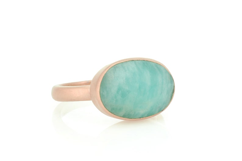 Puede incluir: Un anillo de oro rosa con una gran piedra preciosa ovalada de color verde. La piedra preciosa es de color verde claro y tiene un patr&oacute;n de m&aacute;rmol.