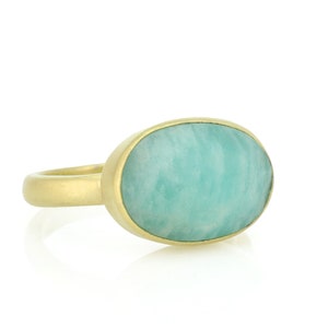 Puede incluir: Un anillo de oro con una gran piedra preciosa ovalada de color verde. La piedra preciosa tiene un patr&oacute;n de remolino.