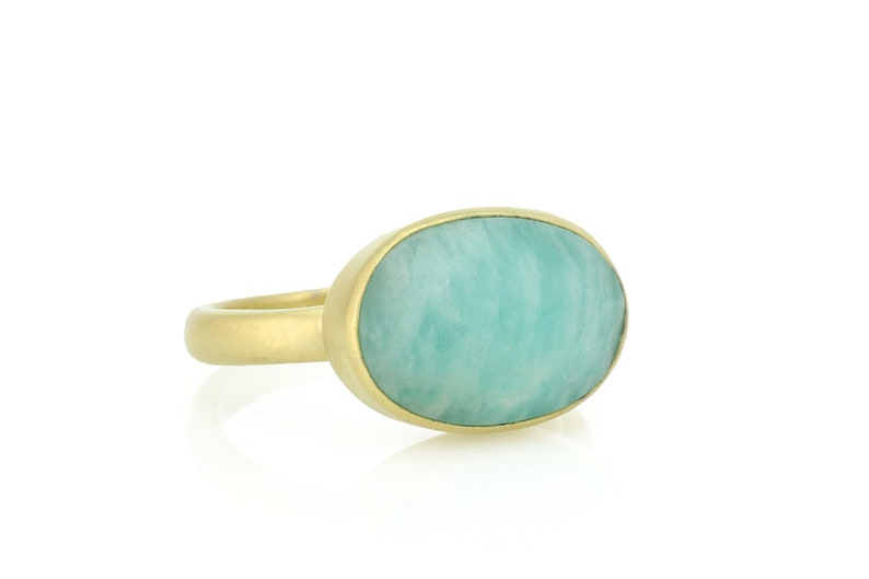 Puede incluir: Un anillo de oro con una gran piedra preciosa ovalada de color verde. La piedra preciosa tiene un patr&oacute;n de remolino.