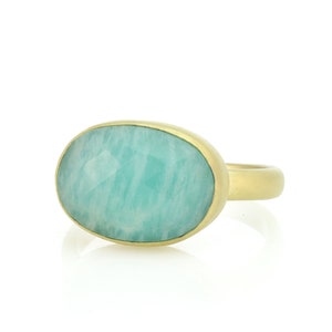Puede incluir: Un anillo de oro con una gran piedra preciosa ovalada de color verde. La piedra preciosa es de color verde claro y tiene una superficie lisa y pulida.