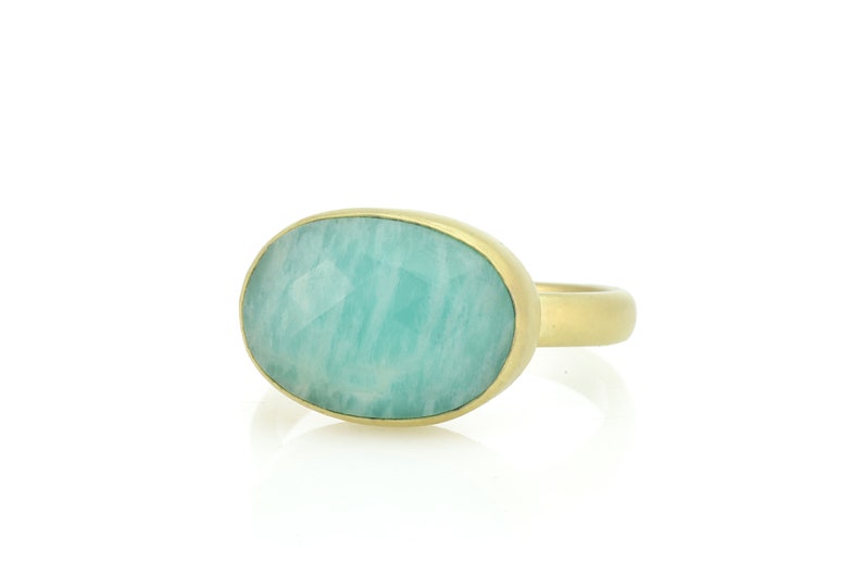 Puede incluir: Un anillo de oro con una gran piedra preciosa ovalada de color verde. La piedra preciosa es de color verde claro y tiene una superficie lisa y pulida.