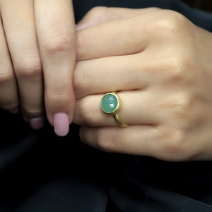 May include: A gold ring with a green oval gemstone. The ring is on a person's finger.