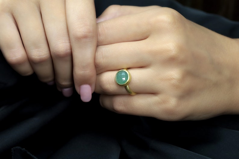 May include: A gold ring with a green oval gemstone. The ring is on a person's finger.