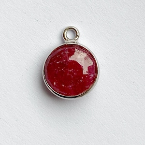 May include: A round, red gemstone pendant with a silver setting and a loop for attaching a chain.